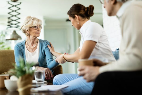 Female nurse communicating with senior woman while being in home visit. Focus is on senior woman.